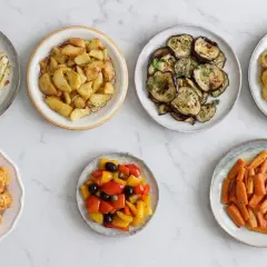 Sette piatti di verdure in friggitrice ad aria: finocchi, patate, melanzane, zucchine, cavolfiore, peperoni e carote.
