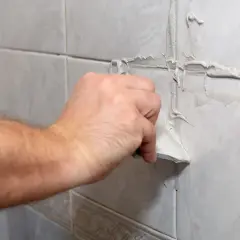 Main tenant utilise une spatule pour refaire le joint du carrelage mural.