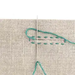 Close-up of a needle and teal thread being used to sew a buttonhole on beige fabric. Stitches are visible along the edges of the cut.