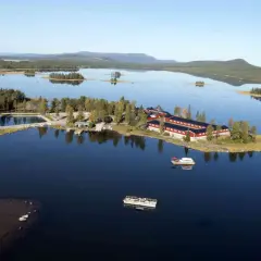 Vacker vy över en sjö med röda byggnader och båtar vid **kraja Arjeplog**.