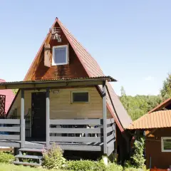 Drewniany olchowiec nad Soliną, z czerwonym dachem i werandą, otoczony zielenią.