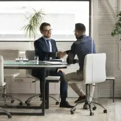 Dwóch mężczyzn w garniturach ściska sobie dłonie przy biurku w nowoczesnym biurze.