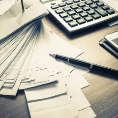 Stos dokumentów, kalkulator i długopis na biurku. Może to być biuro Svea Ekonomi na Cyprze, gdzie analizuje się finanse.