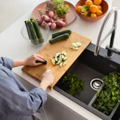 Mężczyzna kroi cukinię na desce obok czarnego zlewu z kranem i natką pietruszki.