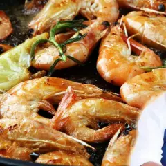 Gambones a la plancha dorados y jugosos, con limón y romero. Un chef sonriente los presenta.