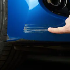 Dito si vede come riparare graffi auto. Un dito indica profondi graffi su un'auto blu vicino alla ruota.