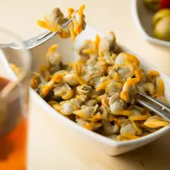 Un plato de berberechos, pequeños moluscos marinos, listos para disfrutar. Se ven deliciosos junto a un vaso de bebida y aceitunas.