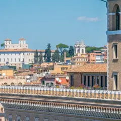 Vue panoramique de Rome, avec la Villa Médicis et ses jardins en arrière-plan, sous un ciel bleu clair.