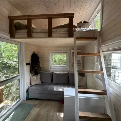 Clevere tiny house bett ideen: ein gemütliches Hochbett über einer Couch, mit Leiter und Fensterblick ins Grüne.