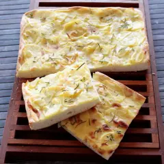 Focaccia con lievito istantaneo, ricoperta di patate sottili e rosmarino, tagliata a fette su un tagliere di legno.