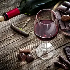 Ein Glas Rotwein und verschiedene Schokoladenstücke auf Holztisch. Ein Korkenzieher liegt daneben.