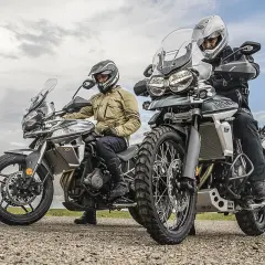 Dos motociclistas con cascos y equipo de aventura listos para explorar caminos y **trail asfalticas** bajo un cielo nublado.