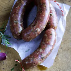 Frische italienische Bratwurst Salsiccia, bereit für ein köstliches Rezept. Rosmarin und Knoblauch liegen daneben.