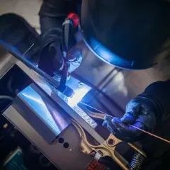 Precyzyjne spawanie TIG metalowych elementów. Ręce w rękawicach trzymają palnik i drut spawalniczy, tworząc jasny łuk.