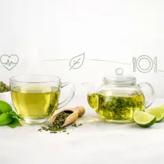 Parująca filiżanka zielonej herbaty, dzbanek z naparem, liście i limonki. Czy zielona herbata pobudza? Z pewnością dodaje energii do zdrowego stylu życia.