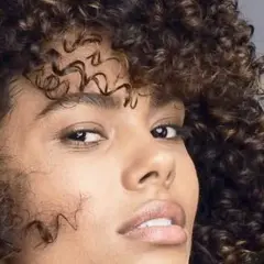Mujer con cabello rizado y oscuro, mostrando cómo nutrir el pelo para un brillo saludable.