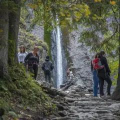 Grupa turystów podziwia wodospad w Tatrach. To idealne miejsce na odkrywanie najpiękniejszych szlaków w Tatrach dla początkujących.
