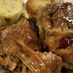 Succulento agnello al forno, dorato e lucido, servito con patate arrosto e una cremosa salsa verde.