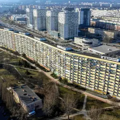 Długi, falisty budynek mieszkalny, znany jako falowiec gdańsk, otoczony zielenią i innymi blokami.