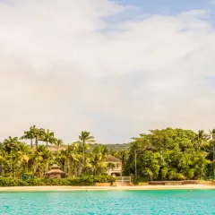 Tropikalna plaża z palmami i willami nad turkusowym morzem.