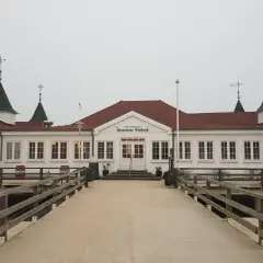 Historyczna budowla na molo w Ahlbecku, z charakterystycznymi zielonymi dachami i białymi ścianami, zaprasza do spaceru.