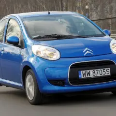 Niebieski Citroen C1 pędzi po drodze, odbijając światła miasta w swoich błyszczących reflektorach.