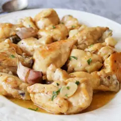 Sabroso pollo al ajillo servido en un plato blanco, con trozos de pollo dorados y jugosos, cubiertos con una salsa de ajo y perejil.
