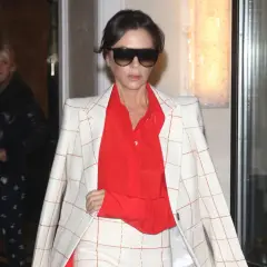 Victoria Beckham, con un traje de cuadros blanco y naranja y camisa roja, sale de un edificio.