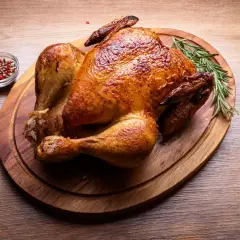 Złocisty, cały kurczak z airfryer na desce, udekorowany rozmarynem. Obok miseczka z pieprzem i cytryną.