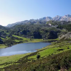 Lago en un valle montañoso verde con picos rocosos al fondo.