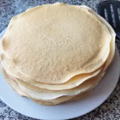 Stos cienkich, złotych placków, idealne ciasto na krokiety, leży na białym talerzu obok łopatki.