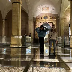 Due ragazze esplorano il Palazzo Madama, con un pavimento in vetro che rivela antiche rovine sottostanti.