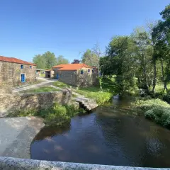 Casas de piedra con tejados rojos y ventanas azules junto a un río. Un lugar idílico que ver en Vila de Cruces.