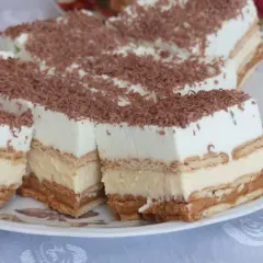 Szybkie ciasto bez pieczenia z budyniem i herbatnikami, przełożone kremem i posypane wiórkami czekoladowymi. Idealne na deser!