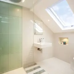 Moderno baño con ducha de cristal verde, lavabo flotante y tragaluz. Ideas para como decorar un baño con estilo y luz natural.
