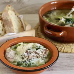 Two bowls of hearty Italian soup with greens and meat, served with crusty bread in a wooden crate.