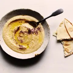 Un bol de houmous onctueux, arrosé d'huile d'olive et saupoudré d'épices, prêt à être dégusté avec du pain pita. Une recette houmous simple et savoureuse.