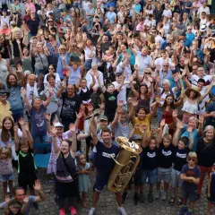 Große Menschenmenge winkt fröhlich bei Brackenheim Veranstaltungen. Ein Mann hält eine Tuba, Kinder und Erwachsene sind begeistert.