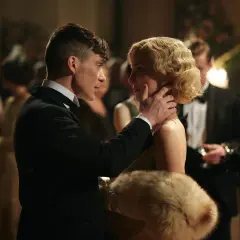 Tommy Shelby czule dotyka policzka Grace, jednej z kluczowych kobiet w świecie Peaky Blinders. W tle widać innych gości balu.