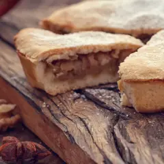 Pyszna szarlotka z jabłkami, posypana cukrem pudrem. Obok orzechy i anyż. Idealna na jesienne popołudnie, gdy zastanawiasz się, czym zagęścić jabłka do szarlotki.