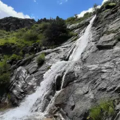Una hermosa cascada en Madrid, cayendo por rocas grises y vegetación verde bajo un cielo azul con nubes blancas.