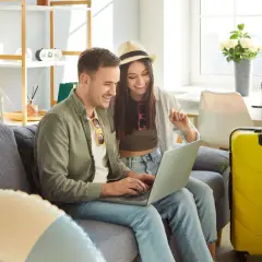 Para planować majówkę i wolne dni, para przegląda ofertę na laptopie, obok walizek.