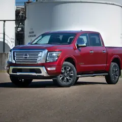 Czerwony Nissan Titan z chromowanymi detalami stoi na asfalcie przed białymi zbiornikami przemysłowymi.