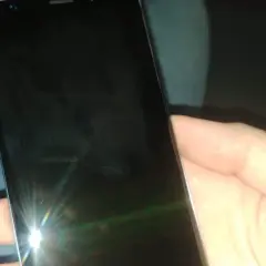 Dłoń trzyma czarny telefon, na którego ekranie widać odbicie światła i ledwo widoczną kreskę na telefonie.