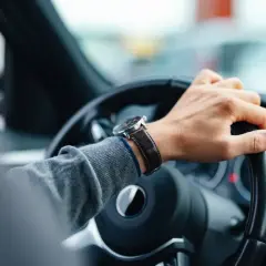 Mano en el volante, reloj de pulsera, tablero de coche. El conductor nota un fallo en la dirección asistida.