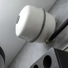 Vue rapprochée du **vase d'expansion chauffage**, élément blanc fixé au mur, avec tuyauterie noire isolée et raccords en laiton.