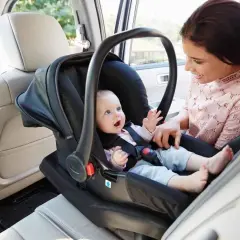 Mama z uśmiechem obserwuje dziecko w foteliku samochodowym. To jeden z rodzajów fotelików samochodowych, zapewniający bezpieczeństwo najmłodszych.