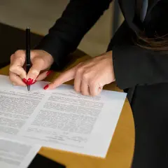 Kobieta z czerwonymi paznokciami podpisuje dokument, który może być wpisem do księgi wieczystej.