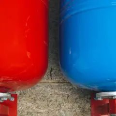 Deux réservoirs, un rouge et un bleu, sont fixés à un mur. Ce sont des éléments essentiels d'un système de chauffage, fonctionnant comme un vase d'expansion.