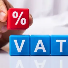 Dłoń układa kostkę z symbolem procentu na kostkach z literami VAT. Rozważasz usługę gastronomiczną a VAT?